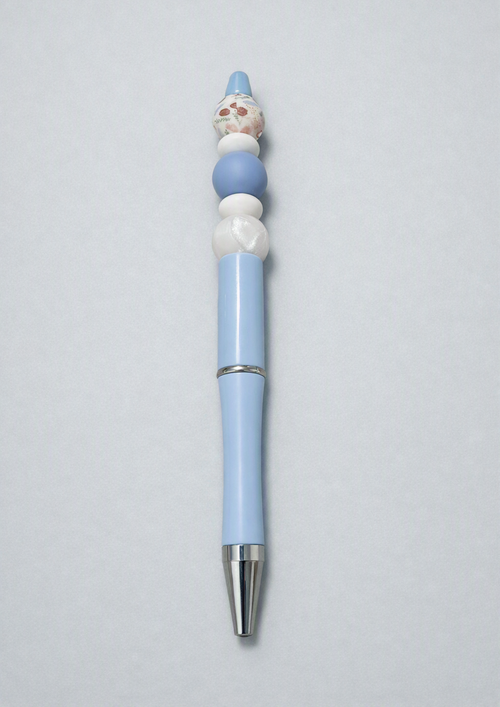 Handmade baby blue beaded ballpoint pen with large white round silicone bead, periwinkle blue silicone bead, cream brown mushroom print round bead with illustrated mushrooms flowers and botanicals on soft blue pen body with silver accent on light gray background